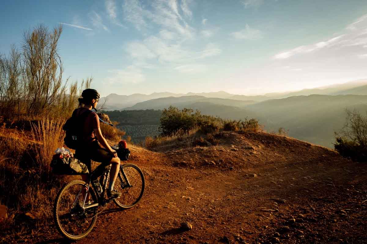 A woman on a bike on the edge of a cliff looking out into the mountains in the distance.